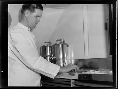 Interior view of aircraft, includes unidentified chef preparing food on board Tasman Empire Airways air boat RMA New Zealand ZK-AME flight to Fiji