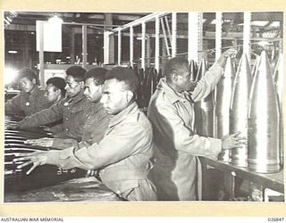 MARIBYRNONG, AUSTRALIA. 1942-10-12. SIX PAPUAN NATIVE SOLDIERS ON A TOUR OF INSPECTION OF THE MUNITION WORKS HANDLE THE HEAVY CALIBRE SHELLS AWAITING DESPATCH TO UNITS IN THE FORWARD AREA