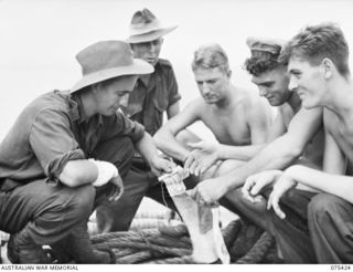 AT SEA. 1944-08-21. A MEMBER OF THE 30TH INFANTRY BATTALION SELLING SOME OF THE TROPHIES WHICH HE CAPTURED FROM THE JAPANESE, TO A MEMBER OF THE CREW OF THE RAN FRIGATE, HMAS "BARCOO" WHILE EN ..