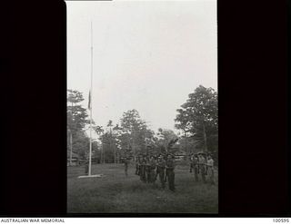 Lae, New Guinea. 1944-07-27. Members of 22 Platoon, F Company, 2/1st Guard Regiment, whose duty it is to guard HQ New Guinea Force, present arms at the sounding of the retreat as the flag is struck ..