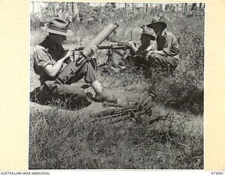 ALEXISHAFEN AREA, NEW GUINEA. 1944-04-27. NX161162 LIEUTENANT J.A. SHIMELD, HEADQUARTERS COMPANY, 30TH INFANTRY BATTALION (1), EXAMINES A CAPTURED VICKERS MEDIUM MACHINE GUN, AT A FORMER JAPANESE ..