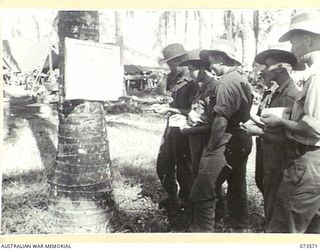 ALEXISHAFEN, NEW GUINEA. 1944-05-27. TROOPS OF HEADQUARTERS 8TH INFANTRY BRIGADE READING THE LIST OF NOMINATIONS FOR THE NEW SOUTH WALES STATE ELECTIONS BEFORE PLACING THEIR VOTES IN A NEARBY TENT ..