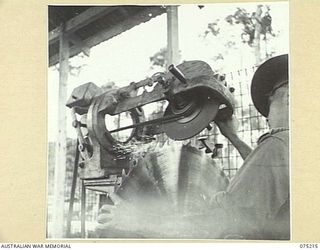 LAE, NEW GUINEA. 1944-08-06. QX19131 LIEUTENANT E.J. BATES, SECTION LEADER, 2/3RD FORESTRY UNIT, SHARPENING A LARGE SOLID TOOTH CIRCULAR SAW IN THE UNIT WORKSHOPS