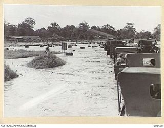 LAE, NEW GUINEA. 1945-10-14. TRAFFIC OF FIRST ARMY ON THE FLOODED ROADWAY WAITING TO CROSS BUTIBUM BRIDGE. FOLLOWING HEAVY RAINS THE BUTIBUM RIVER OVERFLOWED ITS BANKS, FLOODED THE ROAD AND ..