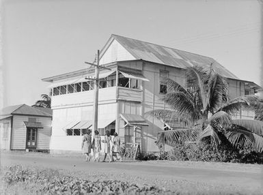 [Women walking past a building in the Pacific Islands]