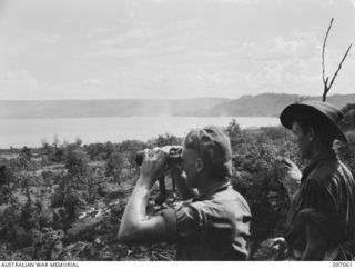 RABAUL, NEW BRITAIN. 1945-09-23. A MEMBER OF 37/52 INFANTRY BATTALION USING A PAIR OF CAPTURED JAPANESE BINOCULARS TO SURVEY SIMPSON HARBOUR. A SECTION OF THE BATTALION IS IN THE AREA GUARDING ..