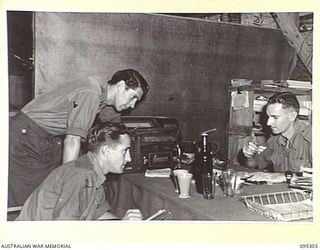 PALMALMAL PLANTATION, JACQUINOT BAY, NEW BRITAIN, 1945-08-15. HEADQUARTERS 11 DIVISION TROOPS IN THE UNIT AMENITIES HUT, WAITING BY THE RADIO FOR NEWS OF VICTORY WITH A BOTTLE OF BEER TO DRINK A ..