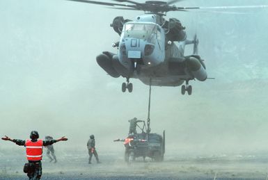 Marines direct a CH-53 Sea Stallion helicopter lowering an M998 High-Mobility Multipurpose Wheeled Vehicle into the staging area during the amphibious assault phase of Exercise RIMPAC 88