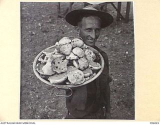 CAPE PUS, WEWAK AREA, NEW GUINEA. 1945-09-07. SERGEANT E. WHITE, 2/14 FIELD COMPANY ROYAL AUSTRALIAN ENGINEERS, WITH A BIG DISH OF FRESHLY MADE ROCK CAKES