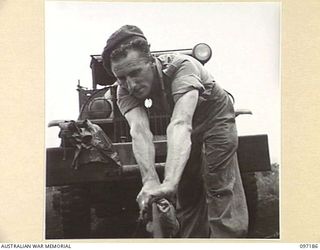 CAPE WOM, NEW GUINEA. 1945-09-27. PRIVATE P.C. FAGAN, DRIVER MECHANIC, 110 BRIGADE ORDNANCE FIELD PARK, DOING ROUTINE MAINTENANCE ON AN EXTENDED WINCH