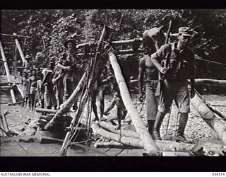 MUBO-SALAMAUA AREA, NEW GUINEA. 1943-07-21. PRIVATE FIRST CLASS LEO SIMON, UNITED STATES ARMY, OF LOS ANGELES, OF THE ALLIED SUPPLY CORPS, IN CHARGE OF A NATIVE FOOD LINE CROSSING THE BITOI RIVER ..