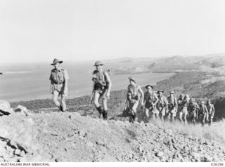 PAPUA. 1942-08. AN AUSTRALIAN INFANTRY PATROL CLIMBS OVER THE STEEP HILLS WITH PORT MORESBY IN THE FAR BACKGROUND