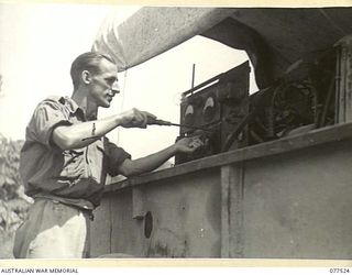 BOUGAINVILLE ISLAND. 1944-12-07. T22111 STAFF SERGEANT N. JUDD OF THE "TASMANIACS" - THE TASMANIA LINES OF COMMUNICATION CONCERT PARTY DOING DAILY MAINTENANCE ON THE UNIT LIGHTING SYSTEM IN ..