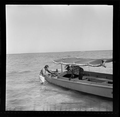 Unidentified man stands in the shallow waters beside a boat with his catch of fish, Nadi, Fiji