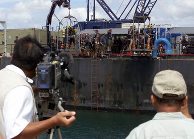 Members of the local news media document US Navy (USN) Divers from Mobile Diving and Salvage Unit One (MDSU-1) conducting training dives alongside the Crowley 450 Barge, in preparation for recovery operations for the Japanese fishing vessel Ehime Maru