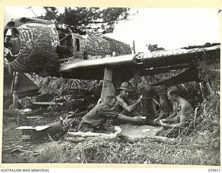 DAGUA, NEW GUINEA. 1945-03-25. MEMBERS OF B COMPANY, 2/2 INFANTRY BATTALION, PLAY CARDS NEAR THEIR "DOOVER" (SHELTER) UNDER THE WING OF A JAPANESE ZERO AT THE AIRSTRIP. IDENTIFIED PERSONNEL ARE:- ..