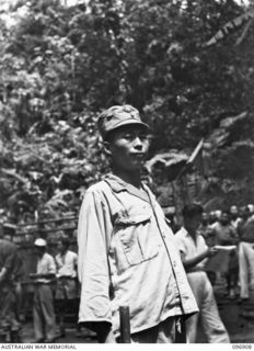 KUMUIA YAMA, RABAUL AREA, NEW BRITAIN. 1945-09-17. A CHINESE SENTRY STANDS GUARD WITH A PIECE OF RED AND WHITE PAINTED WOOD AT THE CHINESE INTERNMENT CAMP. HE IS ONE OF A COMPLETE UNIT BROUGHT FROM ..