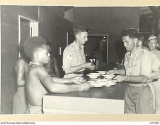 LAE, NEW GUINEA. 1944-11-26. QX396 STAFF SERGEANT E.L. MONEY, ASSISTED BY NATIVES FROM THE AUSTRALIAN NEW GUINEA ADMINISTRATIVE UNIT, SERVING MEALS AT THE 22ND ARMY CANTEEN SERVICES OTHER RANKS ..