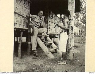 WAMBIT, NEW GUINEA, 1944-03-01. NGX305 WARRANT OFFICER 1, P.M. SWANSON, DEPUTY ASSISTANT DIRECTOR NATIVE LABOUR AT WAMPIT, HEADQUARTERS, COMMANDER ROYAL ENGINEERS (A.I.F.) (1), PICTURED WITH A ..