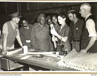 ALEXANDRIA, NSW. 1944-01-24. AUSTRALIAN AND NEW GUINEA ADMINISTRATION UNIT NATIVES WATCHING WOODEN RIFLE COMPONENTS BEING GAUGED FOR ACCURACY OF MACHINING AT SLAZENGER'S FACTORY