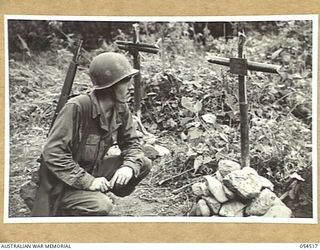 MUBO-SALAMAUA AREA, NEW GUINEA, 1943-07-21. PRIVATE FIRST CLASS D.J. COMMINS, 1ST BATTALION, 162ND INFANTRY, UNITED STATES ARMY, STOPS TO READ THE NOTICES ON THE GRAVES OF QX28016 PRIVATE G.A. ..