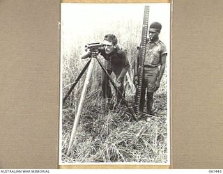 DUMPU, NEW GUINEA. 1943-12-06. VX105243 CORPORAL D. W. A. BAKER OF THE 18TH AUSTRALIAN ANTI-MALARIAL CONTROL UNIT AND A NATIVE ASSISTANT SURVEYING A LINE FOR A DRAIN WHICH WILL BE USED TO EMPTY A ..