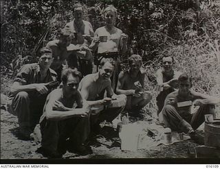 NEW GUINEA. 1943-11-11. FINSCHHAFEN AREA. WEST AUSTRALIAN MEMBERS OF AN A.I.F. UNIT KNOCK OFF FOR A MIDDAY MEAL. JOURNALIST, PRIVATE C. AMMON OF NORTH PERTH, WA (BACK ROW, SECOND FROM LEFT), EATS ..