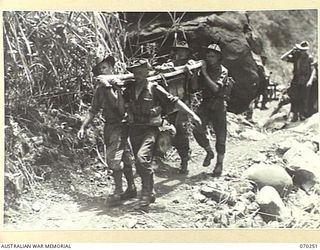 FARIA VALLEY, NEW GUINEA, 1944-02-09. MEMBERS OF THE 11TH FIELD BATTERY, 4TH FIELD REGIMENT, CARRYING A HEAVY BATTERY CHARGER UP THE FARIA VALLEY TO FORWARD POSITIONS. IDENTIFIED PERSONNEL ARE: ..