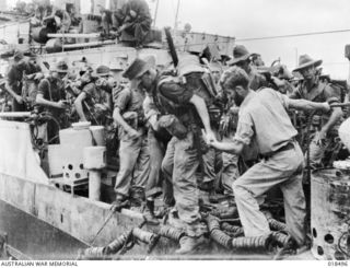 Members of the crew of HMAS Dubbo assisting 6th Australian Division troops into the landing barges for the successful assault on the Wewak Peninsula
