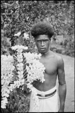 Man holding threaded frangipanni flowers, Samarai, Papua, ca. 1929, 2 / Sarah Chinnery