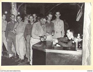 LAE, NEW GUINEA. 1945-11-25. LIEUTENANT COLONEL J.C. MULLALEY, PACIFIC ISLANDS REGIMENT AND OTHER OFFICERS PURCHASING DINNER AND LIQUOR TICKETS FROM CORPORAL J. DRAED AT THE AUSTRALIAN ARMY ..