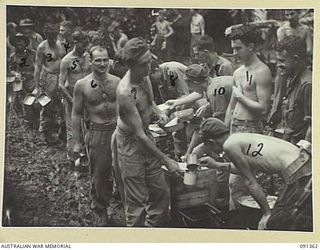 Troops of 9 Infantry Battalion line up in mud for mess parade along the Hatai Track. Identified in the line are (left to right): QX59206 Private (Pte) G A Voight, Qld (in back); QX37924 Pte S C ..