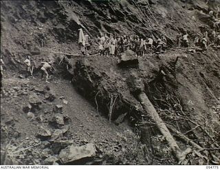 Papua New Guinea. 1943-07-17. Road making in difficult terrain. It took the natives about half-an-hour to roll a huge boulder a few feet to the edge of the mountainside. Boulder is shown poised on ..