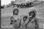 Fainjur: woman with net cap and many strings of trade beads, adolescent girl with barkcloth cap, and child near house