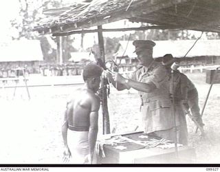 TOROKINA, BOUGAINVILLE, 1945-12-04. MAJOR-GENERAL W. BRIDGEFORD, GENERAL OFFICER IN CHARGE 3 DIVISION, PRESENTING BAGO, A NATIVE SCOUT, WITH A LOYALTY MEDAL, DURING A MEDAL PRESENTATION CEREMONY. ..