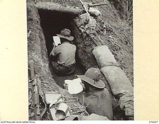 SHAGGY RIDGE, NEW GUINEA. 1944-01-10. QX7442 PRIVATE KNYVETT (1) AND QX3908 LIEUTENANT J.H. MARTIN (2) BOTH OF "A" COMPANY 2/9TH INFANTRY BATTALION ARE READING IN THEIR WEAPON PIT ON THE SUMMIT OF ..