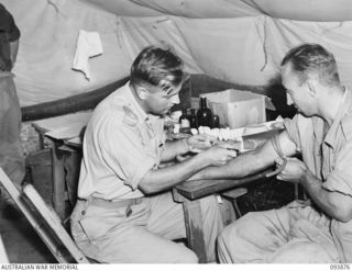 CAPE WOM, WEWAK AREA, NEW GUINEA, 1945-07-11. OFFICER COMMANDING FIELD DETACHMENT LAND HEADQUARTERS MEDICAL RESEARCH UNIT, MAJOR I.C. MACDONALD (1), TAKING A SAMPLE OF BLOOD FROM SAPPER A.H. SMITH, ..