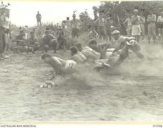 LAE, NEW GUINEA. 1944-06-08. COMPETITORS DIVING INTO BLACK DUST FOR FLAGS DURING A NOVELTY EVENT IN A SPORTS CARNIVAL HELD BY MEMBERS OF THE 2/7TH ADVANCED WORKSHOP AT VOCO BEACH. THE CARNIVAL IS ..