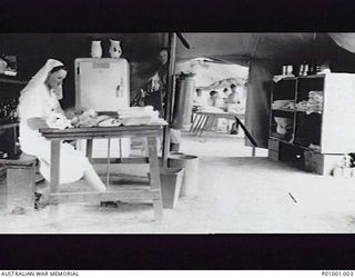 NEW GUINEA? 1943? INTERIOR OF A HOSPITAL TENT WITH A NURSE SEATED AT A TABLE AND PATIENTS LYING ON BEDS SEEN THROUGH THE OPENING. NOTE THE REFRIGERATOR AND THE MAKESHIFT SHELVING FOR LINEN AND ..