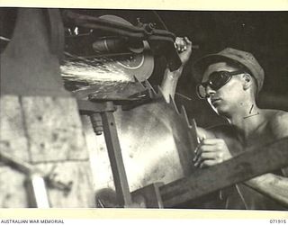 LAE, NEW GUINEA. 1944-03-30. NX154342 LANCE CORPORAL J. RICKETTS (1), SHARPENS TEETH OF A SAW ON A GULLETING MACHINE AT THE 59TH CORPS FIELD PARK COMPANY SAWMILL