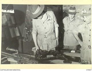 AITAPE, NEW GUINEA. 1945-03-23. LORD WAKEHURST, KCMG, GOVERNOR OF NEW SOUTH WALES IN THE BATTLE ROOM AT HEADQUARTERS 6TH DIVISION INSPECTS PART OF A CAPTURED JAPANESE ANTI- AIRCRAFT RANGE. ..