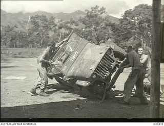 NEW GUINEA. C. 1943. AT AN ADVANCED NEW GUINEA BASE THE PROBLEM OF SWIFT SERVICE TO A JEEP IS SOLVED BY THESE RAAF MOTOR MECHANICS (FITTERS DMT'S) WHO LIE THE VEHICLE ON ITS SIDE. IN CONSTANT MOVES ..