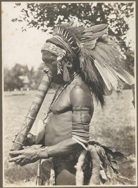 Buna Bay District [man in head dress with a carved wooden object at his mouth] / Frank Hurley