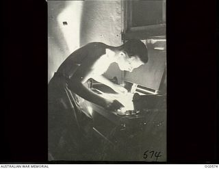 MILNE BAY, PAPUA. 1943-07-31. CORPORAL H. R. RICHARDSON OF PROSPECT, SA, IS BENDING OVER A CONTACT PRINTER EXAMINING NEGATIVES PRIOR TO PRINTING ON BROMIDE PAPER. THE NEGATIVES CAME FROM FILM ..