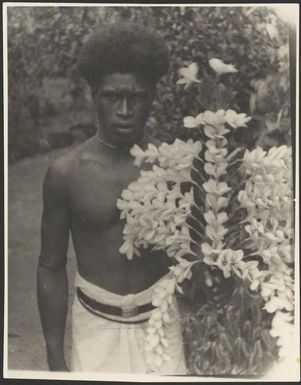 Man holding threaded frangipanni flowers, Samarai, Papua, ca. 1929 / Sarah Chinnery