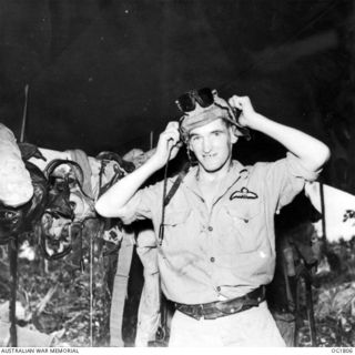 MOMOTE, LOS NEGROS ISLAND, ADMIRALTY ISLANDS, C. 1944-04. 76 KITTYHAWK SQUADRON. BACK IN THE READY HUT FLYING OFFICER H. J. SHELTON, LAUNCESTON, TAS, DOFFS HIS HELMET AND GOGGLES AND HANGS THEM UP ..