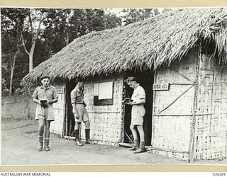TROOPS OF THE 21ST AUSTRALIAN INFANTRY BRIGADE AT A LIBRARY HUT IN THE FORWARD AREA. THE HUT IS BUILT OF INTERWOVEN BAMBOO AND ROOFED WITH KUNAI GRASS