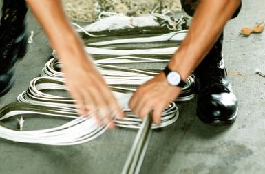 A member of the 8th Mobile Aerial Port Squadron repairs suspension lines on parachute prior to attaching packages to be delivered during Christmas Drop. The annual airdrop is a humanitarian effort providing aid to needy islanders throughout Micronesia during the holiday season