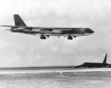 A B-52D Stratofortress aircraft waits beside the runway as a B-52G approaches for landing after completing a bombing mission over North Vietnam during Operation LINEBACKER. The aircraft are from the Strategic Air Command