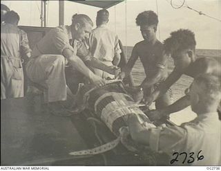 PORT MORESBY, PAPUA. C. 1944. A CASUALTY IN A STOKES LITTER ON BOARD A MOTOR LAUNCH OF THE RAAF RESCUE SERVICE WITH THE HELP OF TWO PAPUAN NATIVE CREW MEMBERS